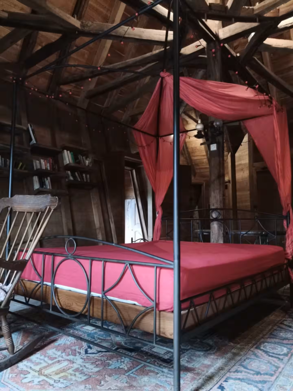 large four poster bed in a room lined with wood and exciting angles, with a ceiling made of radiating wooden beams