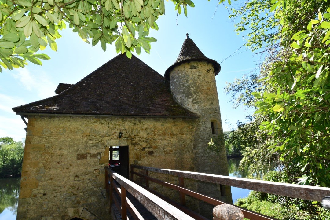 looking along a wooden bridge that enters a stone mill, with turret on the far side