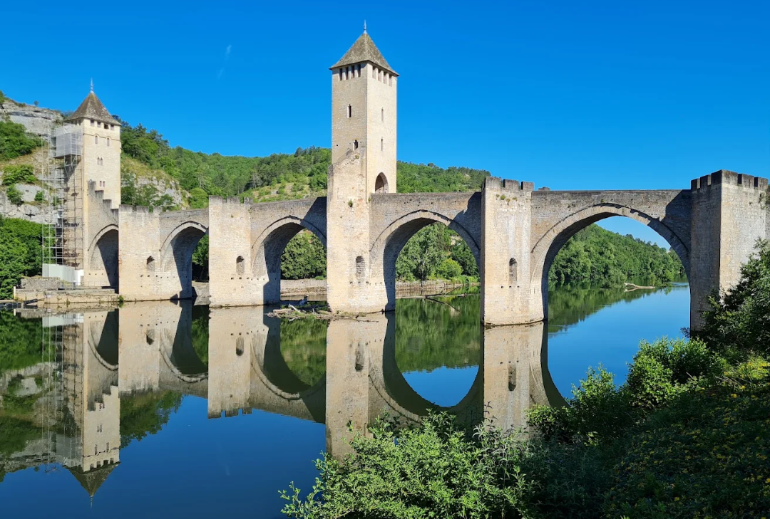 Gleaming stone bridge with medieval tower crosses a river producing a clear reflection