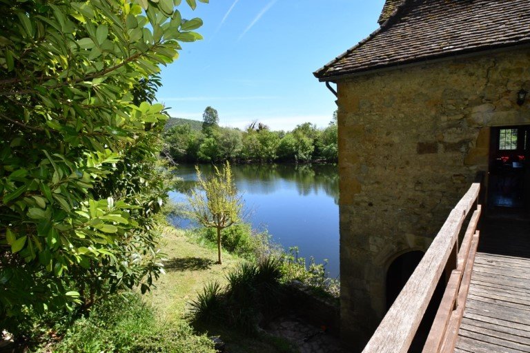 Elevated wooden bridge to a front door in a stone wall. The river flows by on the left.